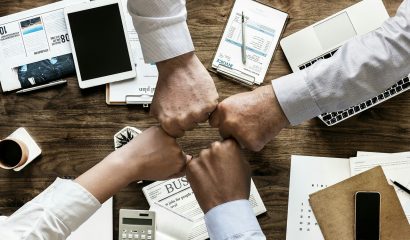 Four people fist bumping above a desk with papers and calcualtors